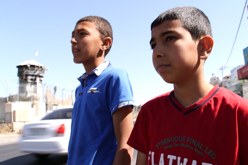 Two boys stand in front of an Israeli watchtower near the entrance to Aroub camp