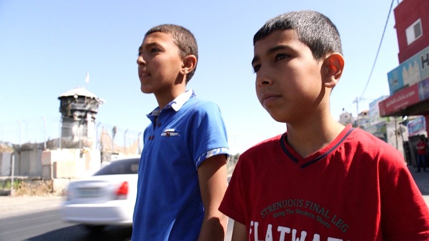 Two boys stand in front of an Israeli watchtower near the entrance to Aroub camp