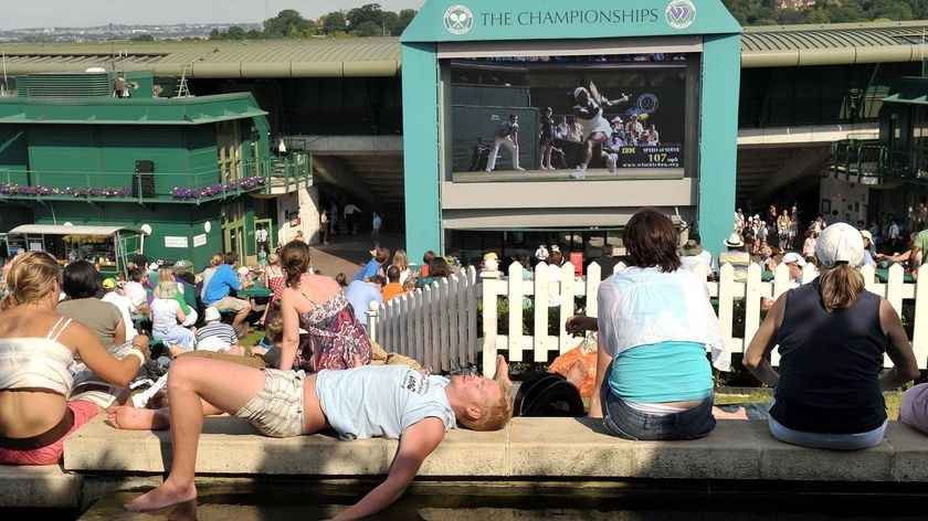 Tennis fans cool themselves down beside a large television screen at Wimbledon