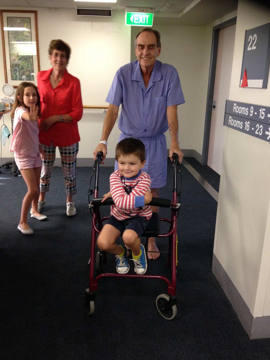 Keith Langley walks on a frame in hospital with his grandson riding on the frame.