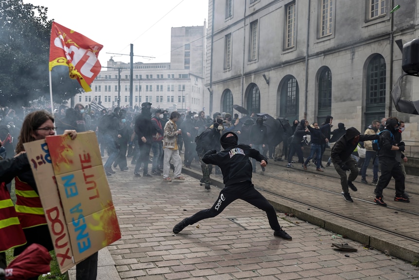 a protester dressed in black throws a stone as protesters gather in Nantes