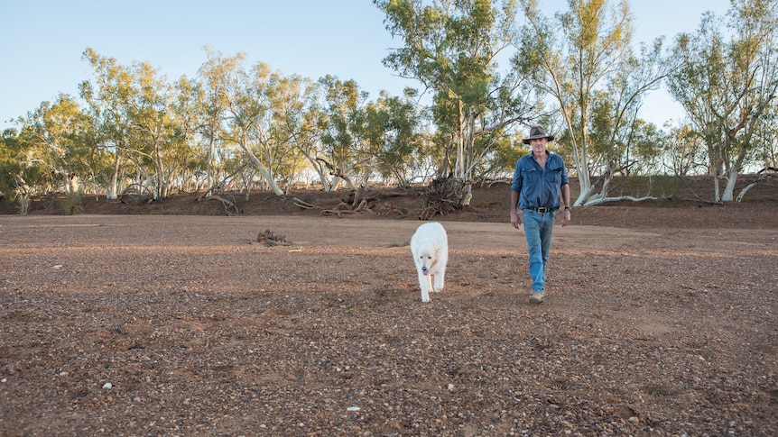 A man in a dry paddock standing next to a dog.