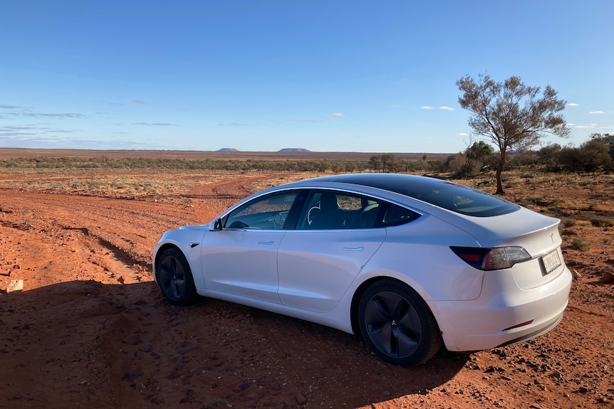 A white car parked on red dirt, the desert stretching out around it