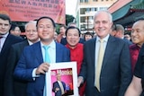Huang Xiangmo stands with  Malcolm Turnbull in front of a crowd holding a picture of Mr Turnbull.