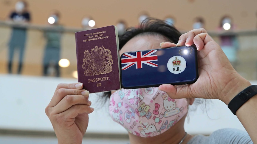 A woman holds a British National Overseas passport and a phone with the HK flag on it while wearing a pink hello kitty face mask