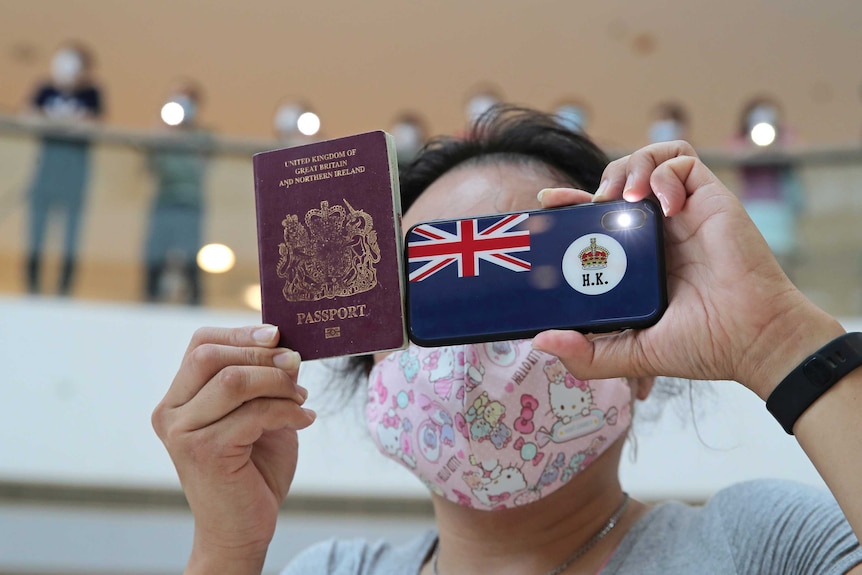 A woman holds a British National Overseas passport and a phone with the HK flag on it while wearing a pink hello kitty face mask