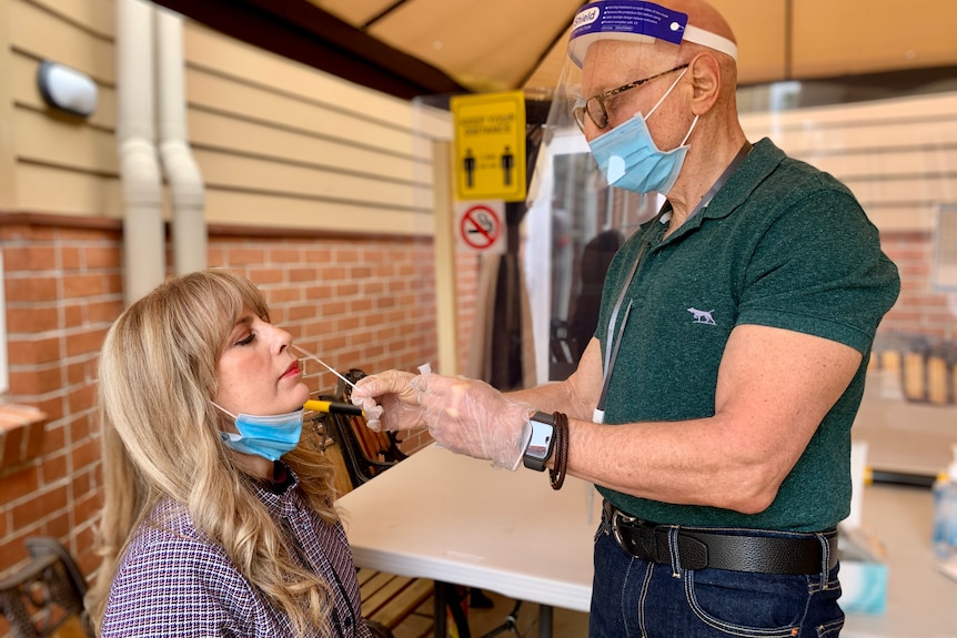 a woman getting a swab up her nose by a doctor in PPE