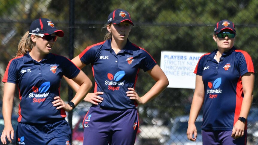 three females cricketers standing in the middle of an oval during training