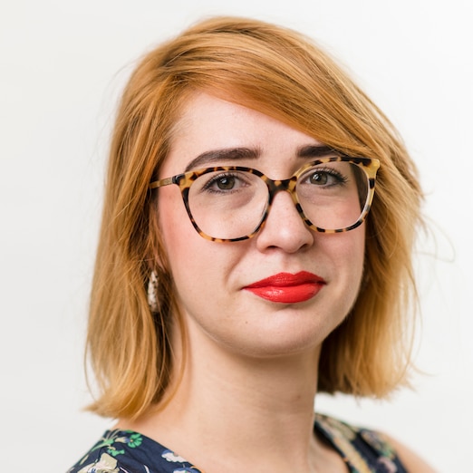 Sabine Wolff faces the camera on a plain white background, wearing round tortoiseshell glasses
