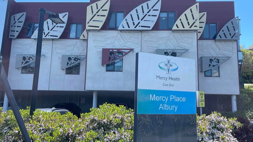 A sign that reads "Mercy Place" in front of a large building.