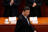 Xi Jinping walks past a row of clapping men wearing face masks.