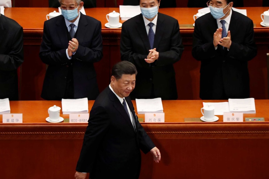 Xi Jinping walks past a row of clapping men wearing face masks.