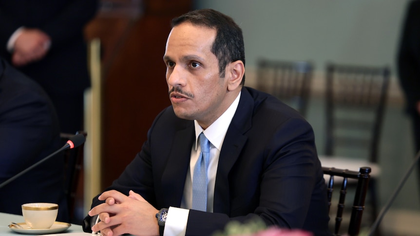 Sheikh Mohammed bin Abdulrahman Al-Thani sits with his hands folded at a table in front of a microphone. 