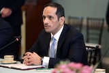 Sheikh Mohammed bin Abdulrahman Al-Thani sits with his hands folded at a table in front of a microphone. 