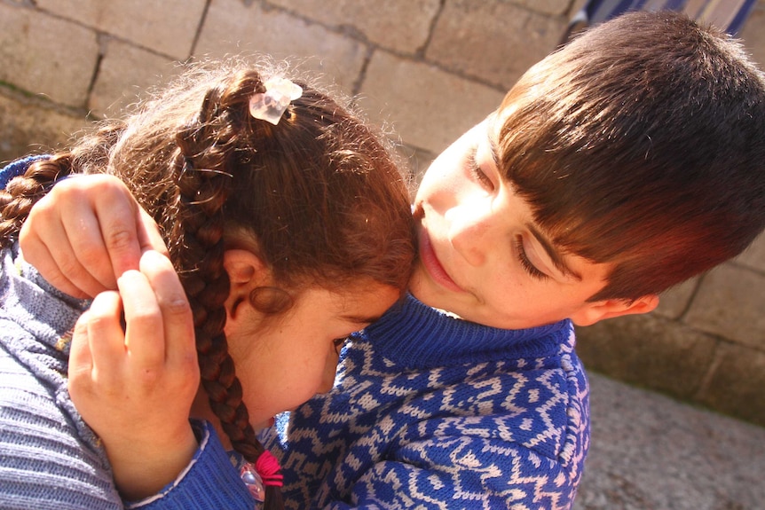 A boy puts a daisy chain around a girls neck.