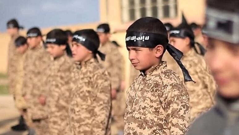 Children stand in a line wearing military uniforms and Islamic State head bands.