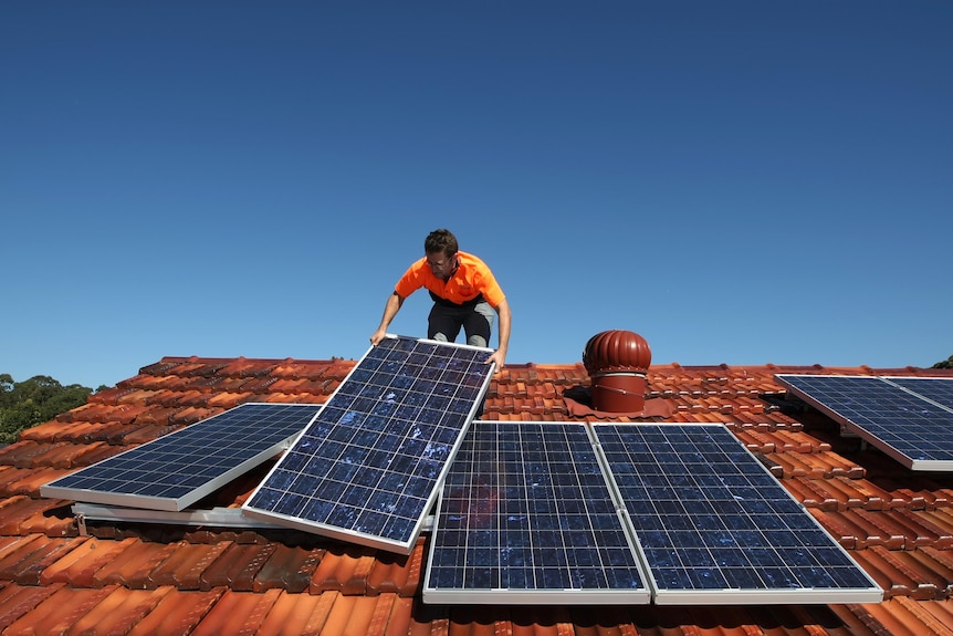 A solar system installer adjusts solar panels on the roof of a house.
