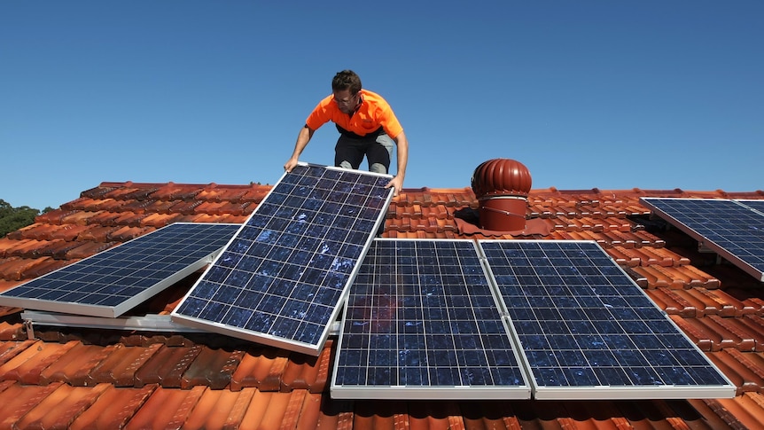 A solar system installer adjusts solar panels on the roof of a house.