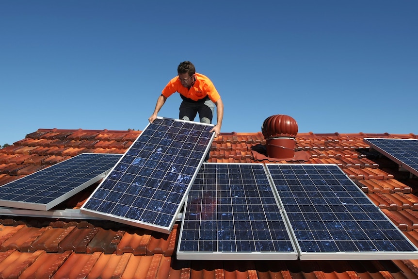 A solar system installer adjusts solar panels on the roof of a house.