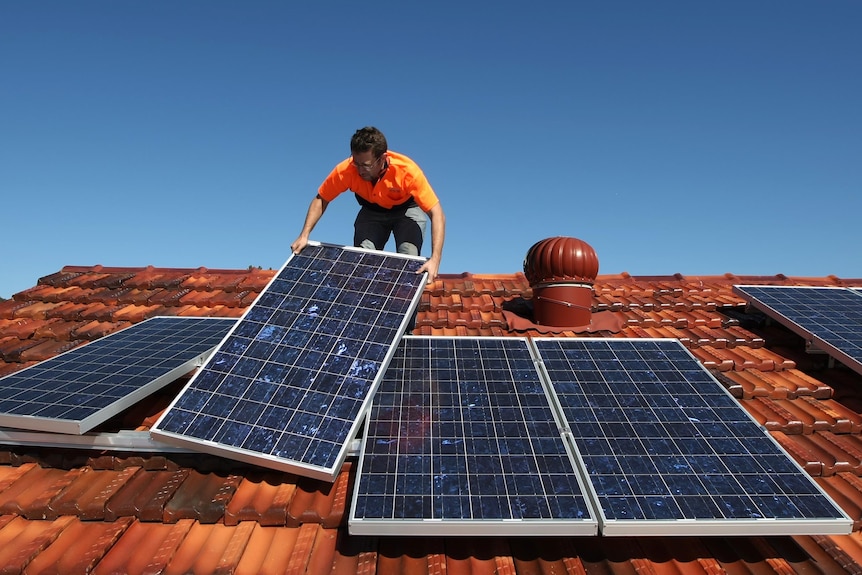 A solar system installer adjusts solar panels on the roof of a house.