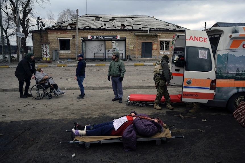 A woman lies on a stretcher in front of an ambulance