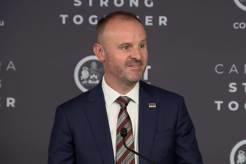 A man in a suit speaks at a podium.