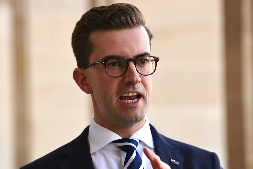 Opposition MP Zak Kirkup speaks on the steps of WA Parliament. He wears a blue suit and glasses.