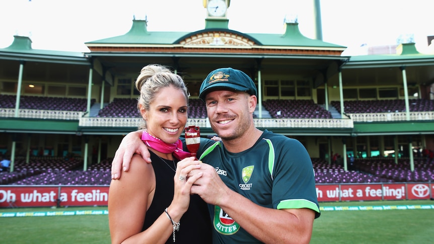 A woman in black and a man in green hold a small urn and smile at the camera.