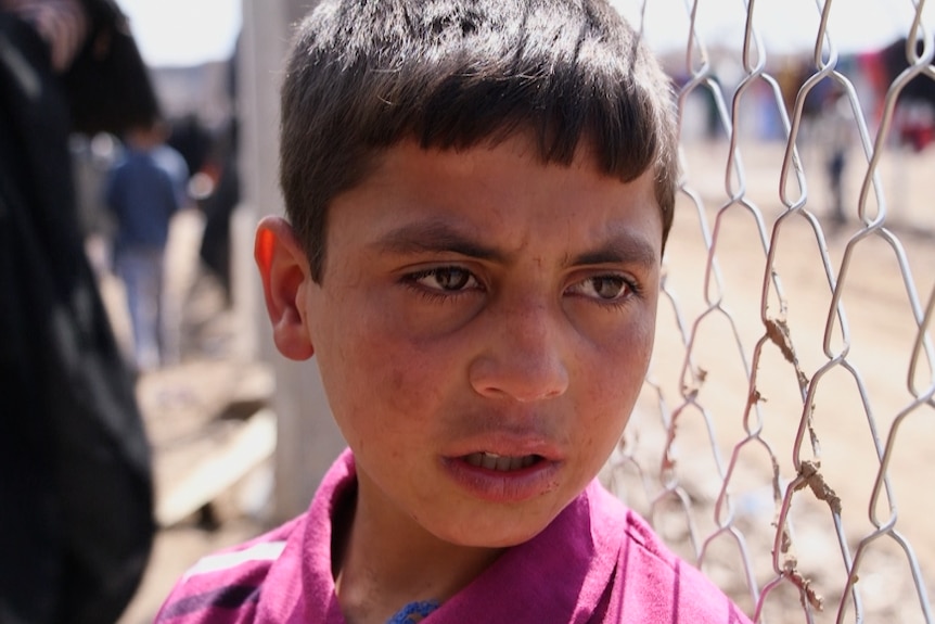 A boy stands by a chain link fence in a Mosul refugee camp