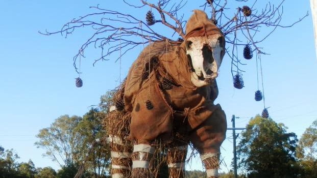 A scarecrow shaped like a deer, made of star pickets, straw, hessian bags and cow skull with branches and pine cones as antlers