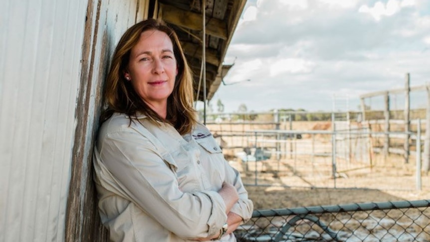 Woman leans on shed looking determinedly at camera