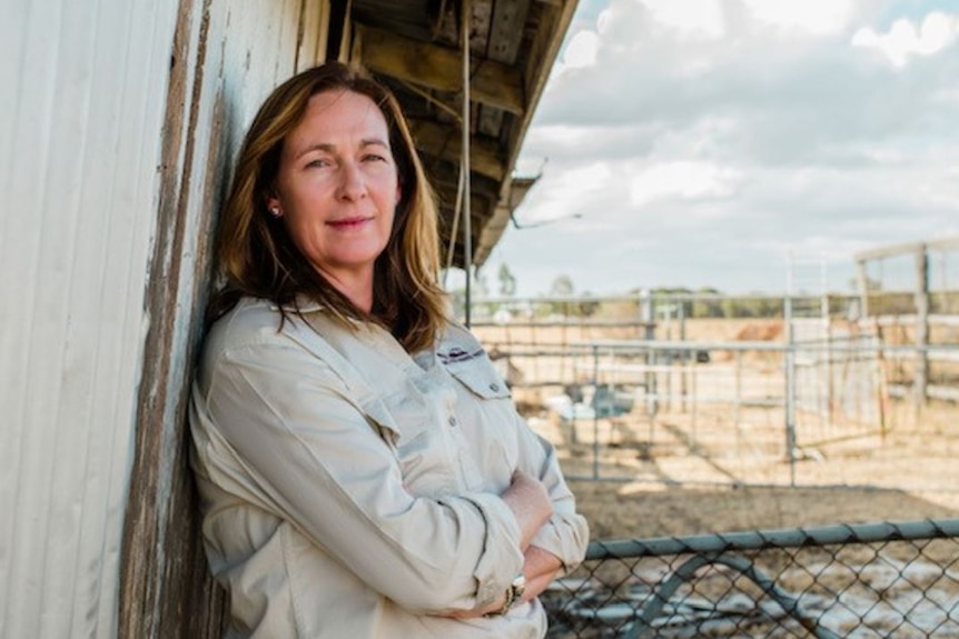 Woman leans on shed looking determinedly at camera