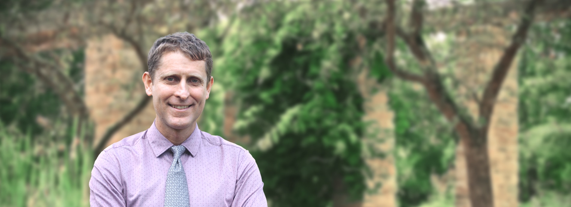 um homem de camisa roxa e gravata cinza sorrindo