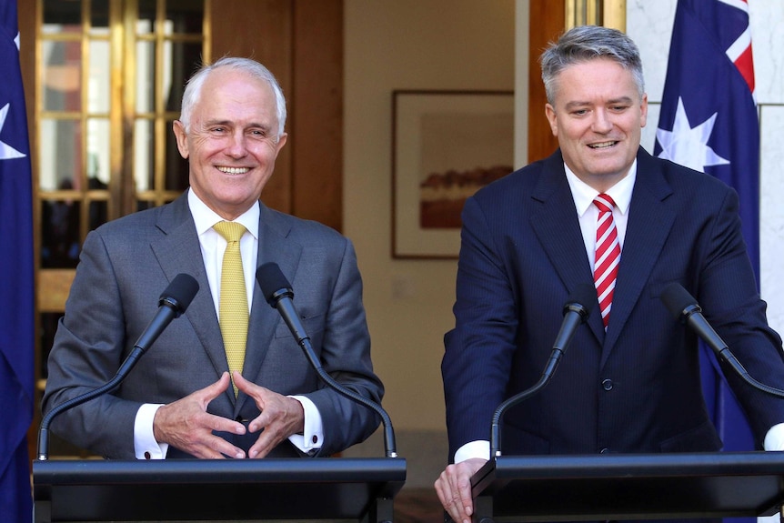Front on view of Malcolm Turnbull and Mathias Cormann smiling at side-by-side lecterns.