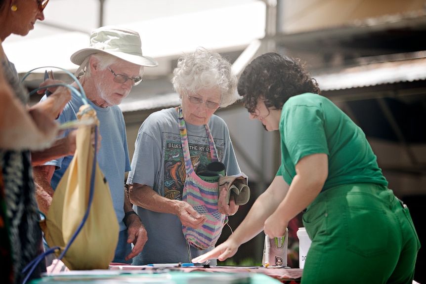 An elderly couple signing a petition while talking to another woman, outside on a sunny day.