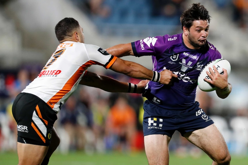 A Wests Tigers NRL player turns to is left as he attempts to tackle a Melbourne Storm opponent.
