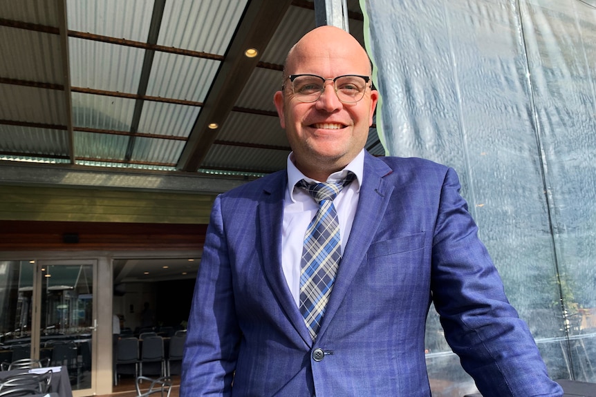 A smiling, bespectacled man in a stylishly tailored suit.