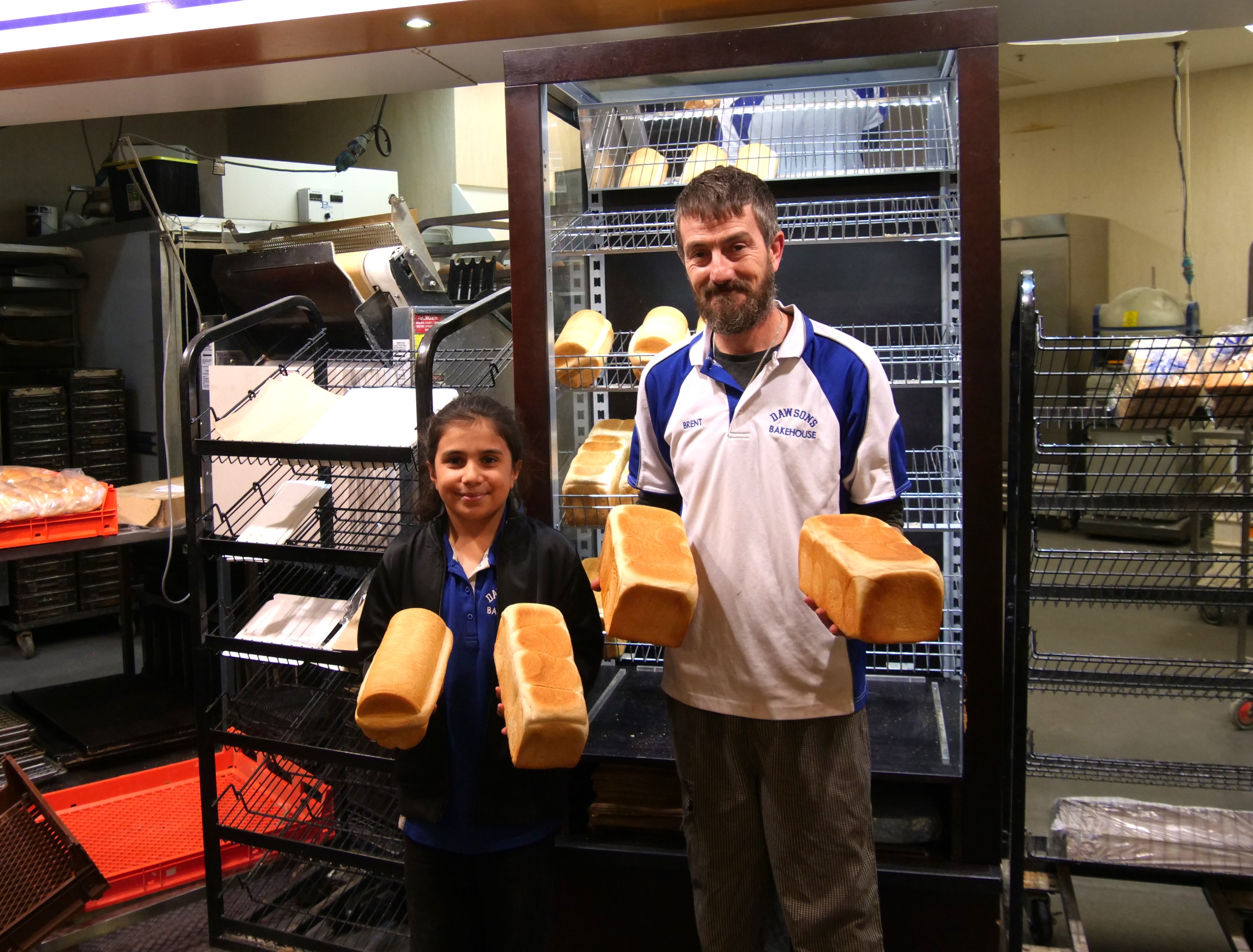 A man and girl stand with bread loaves in their hands.