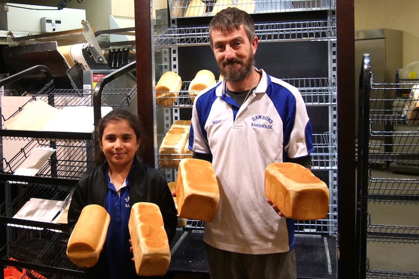 A man and girl stand with bread loaves in their hands.