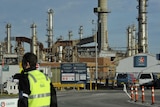 A man in fluoro yellow stands outside a gate of a large oil refinery with the word Caltex on its signage