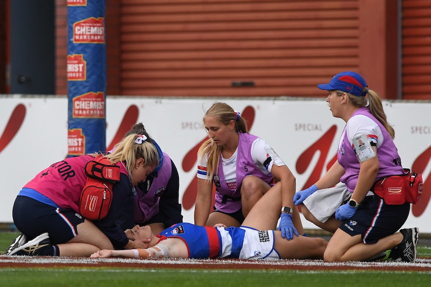 Bulldogs AFLW player Kirsten McLeod is attended to by a doctor and physios as she lies on the ground