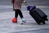 A woman wheeling a suitcase with two plastic bags on her feet.