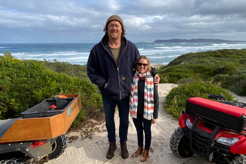 Longley stands towering over woman standing in sand dunes with beach in background.