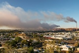 An image showing two mining stacks both expelling dark plumes of smoke over a town.