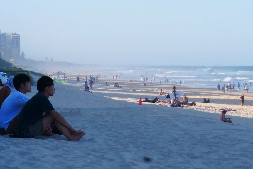 A shot of a Queensland city beach with plenty of people relaxing in front of the surf.