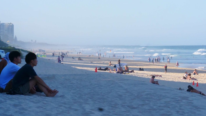 A shot of a Queensland city beach with plenty of people relaxing in front of the surf.