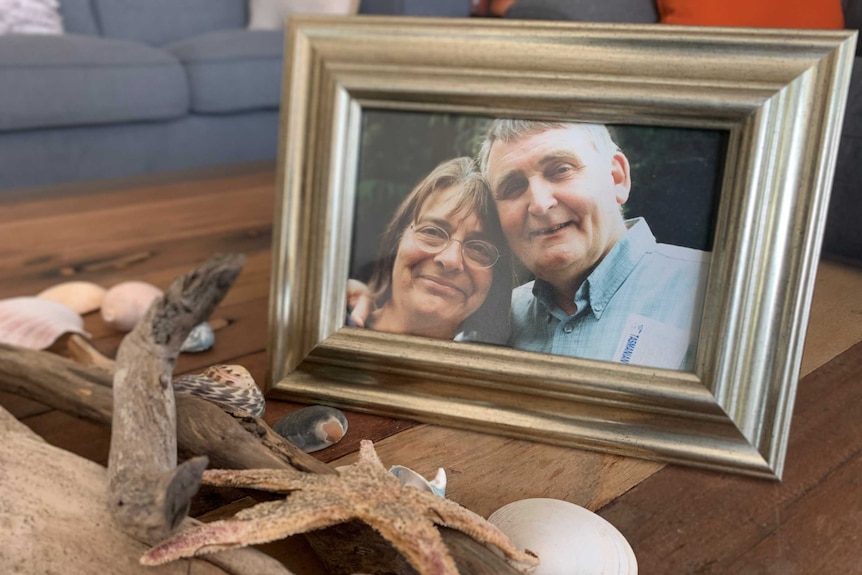 A photograph of a man and woman in a photoframe on a coffee table, with sea shells in the foreground.