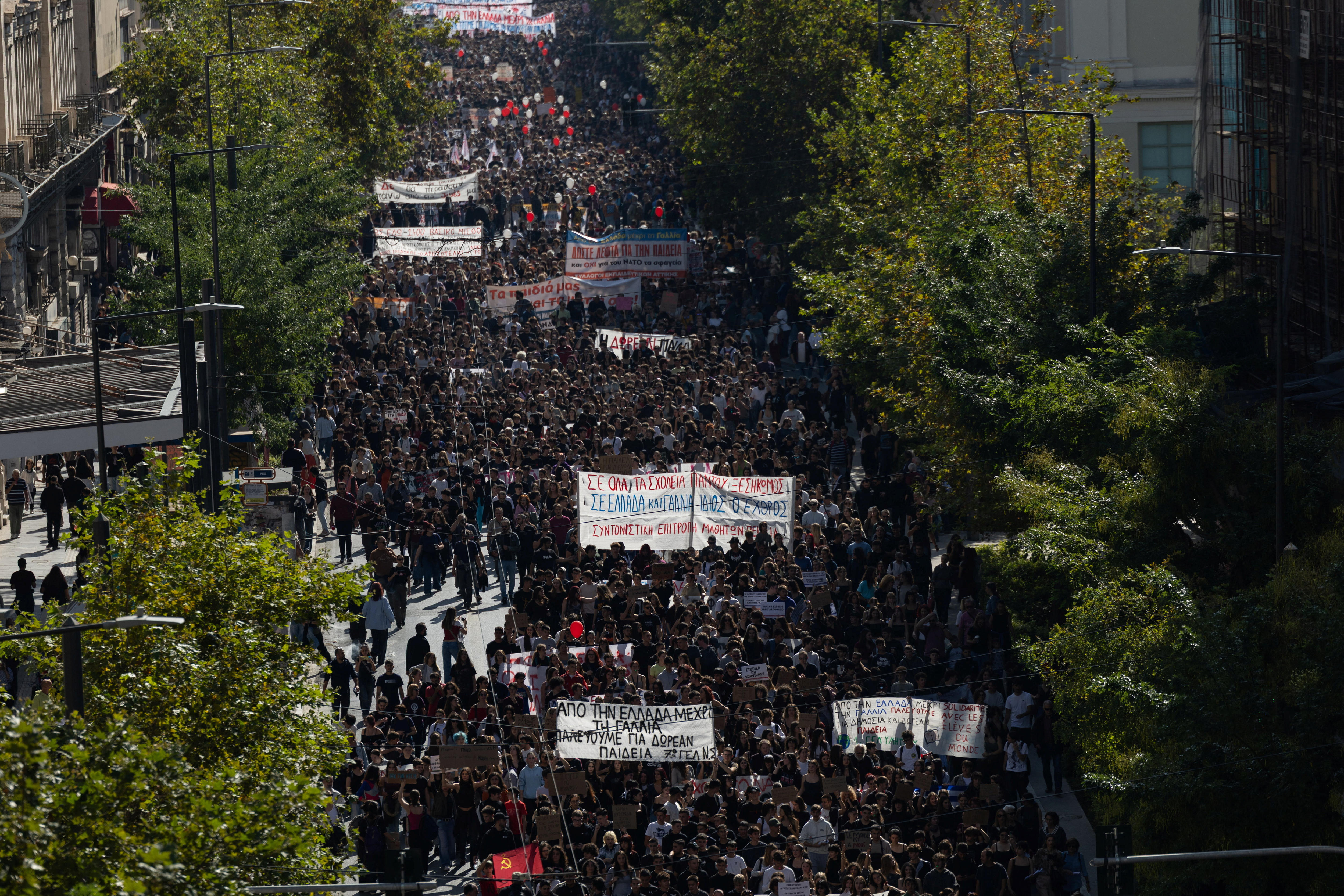 A large crowd of people walking through the streets of Athens holding protest signs