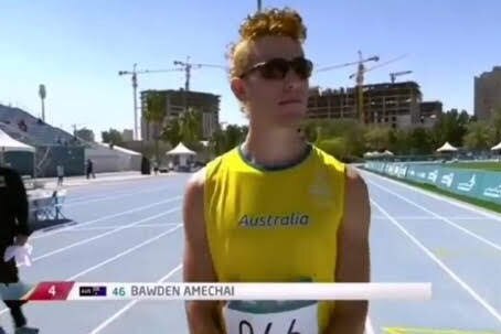 A young male runner wearing a yellow singlet with the word Australia,  and a race bib, stands on a running track.