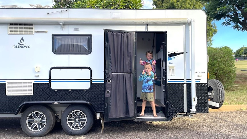 two children stand in the doorway of a cravan with their thumbs up